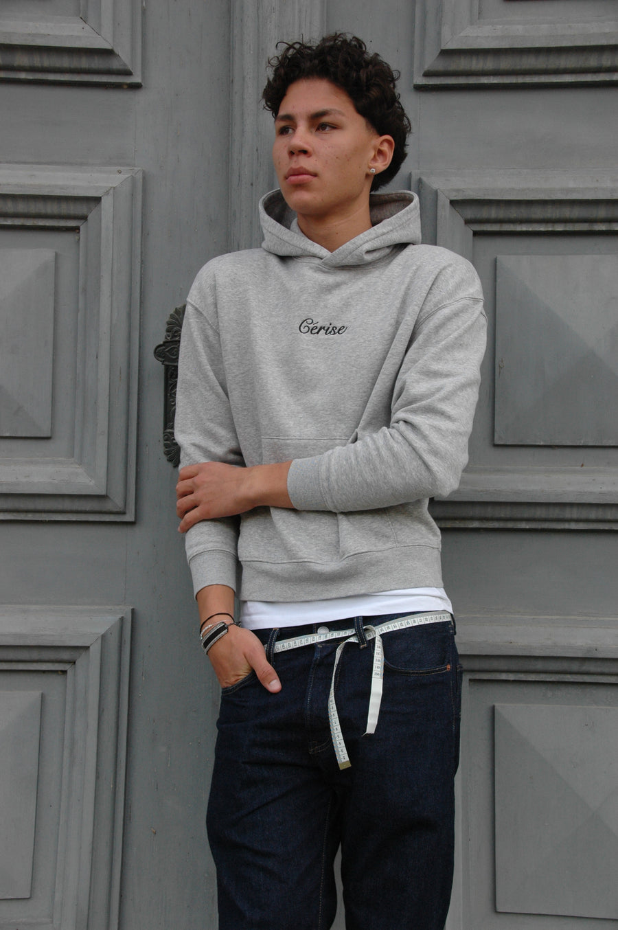 Model im grauen Cérise Hoodie Léopard mit verschränkten Armen vor einer grauen Paneeltür