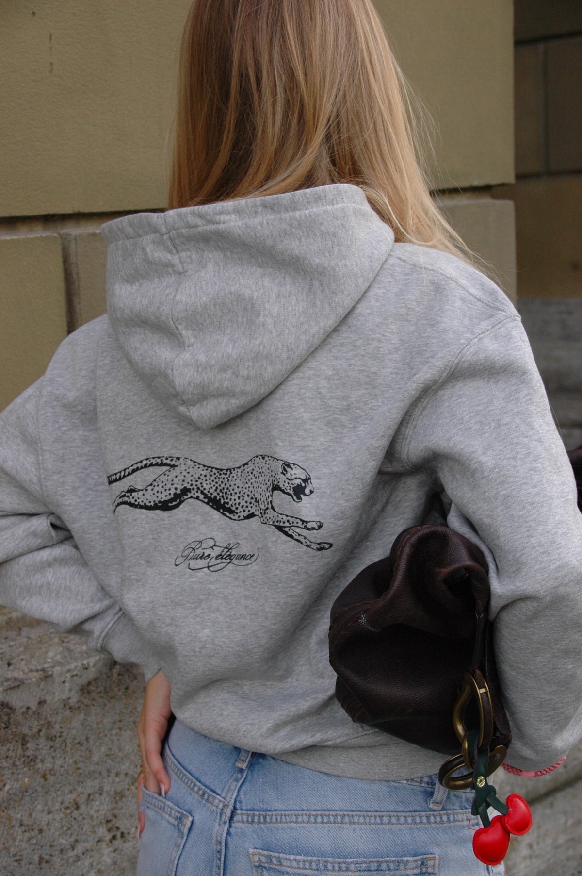 Rückansicht eines Models im grauen Hoodie Léopard mit schwarzem Leoparden-Print, eine Tasche unter dem Arm