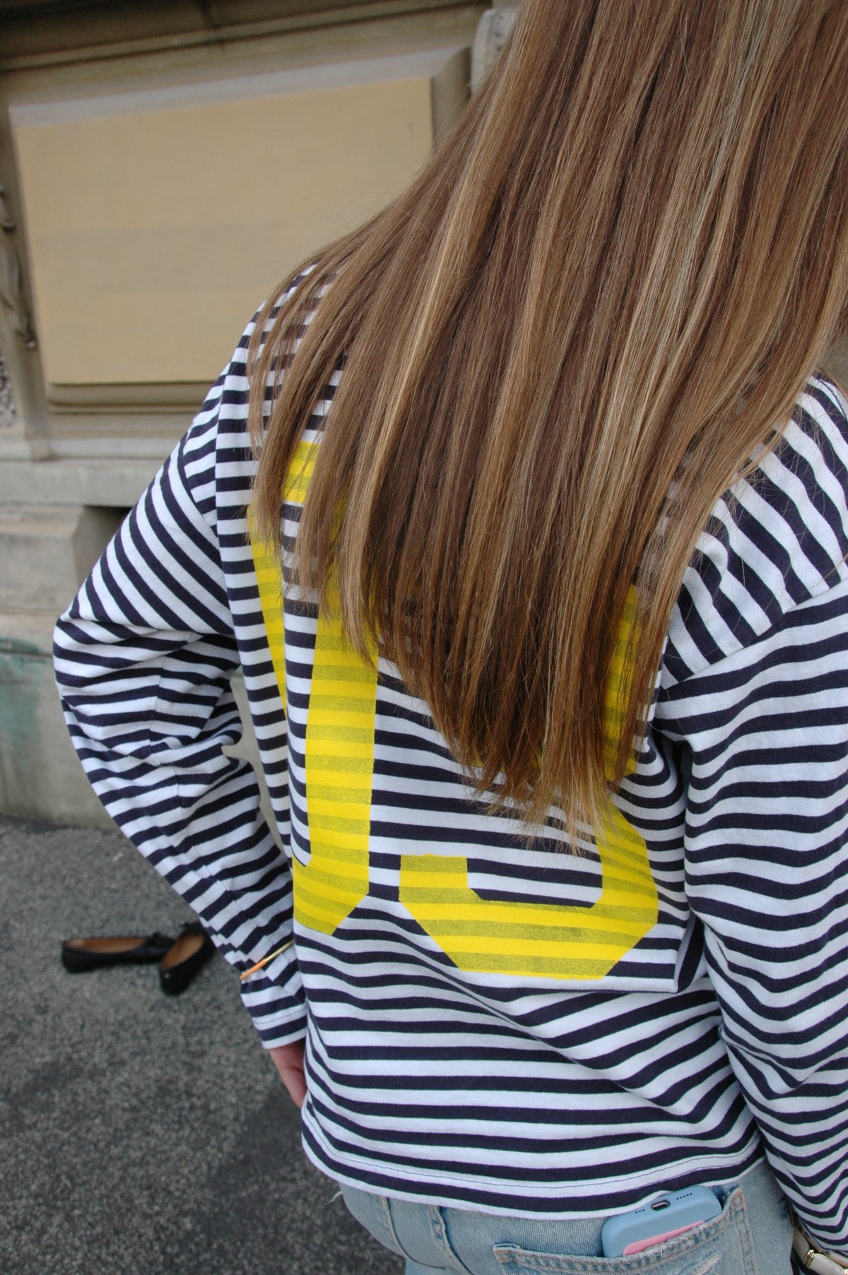 Rückansicht eines Models mit langen Haaren im blau-weiß gestreiften Langarmshirt O-Three mit gelber 03 auf dem Rücken